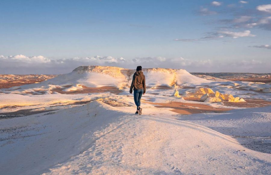 Woman walking across a snow-white landscape in the White Desert, perfect for an Egypt Desert Adventure.