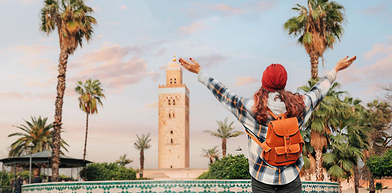 Young woman celebrating reaching Koutoubia Mosque in Marrakech with open arms enjoying her trip to Morocco