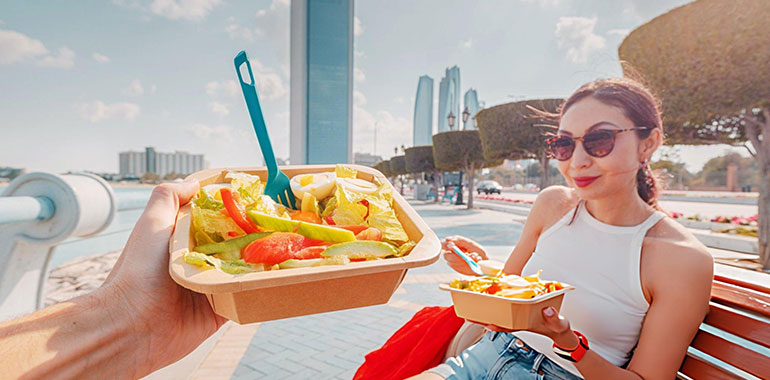 Young woman eating a healthy takeaway salad on a bench in Abu Dhabi corniche street
