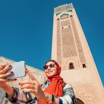 Young-woman-tourist-taking-selfie-with-smartphone-in-front-of-Hassan-II-Mosque-in-the-Casablanca-Morocco