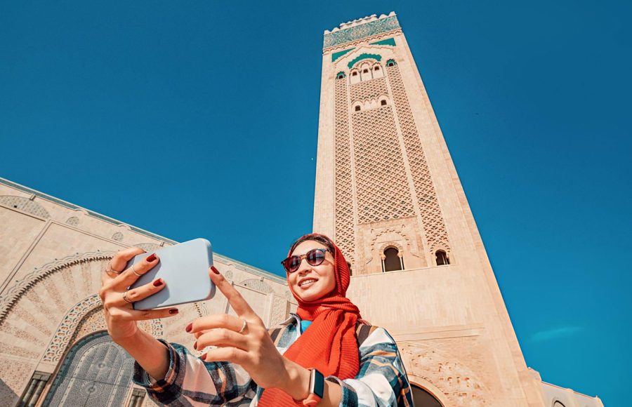 Young-woman-tourist-taking-selfie-with-smartphone-in-front-of-Hassan-II-Mosque-in-the-Casablanca-Morocco
