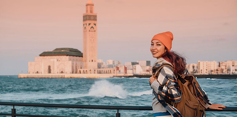 Young woman tourist with backpack enjoying the view of Hassan II Mosque in Casablanca Morocco during a beautiful sunset