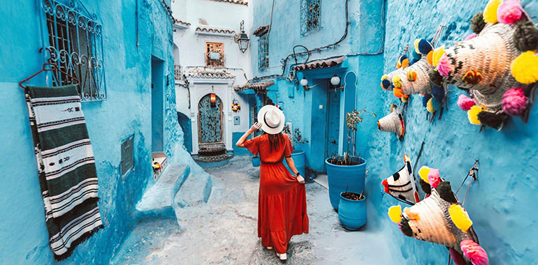 Young woman with red dress visiting the blue city Chefchaouen Marocco