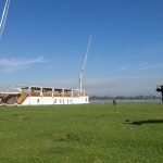 The Zekrayaat Dahabiya docked near a green pasture with a cow in the foreground.