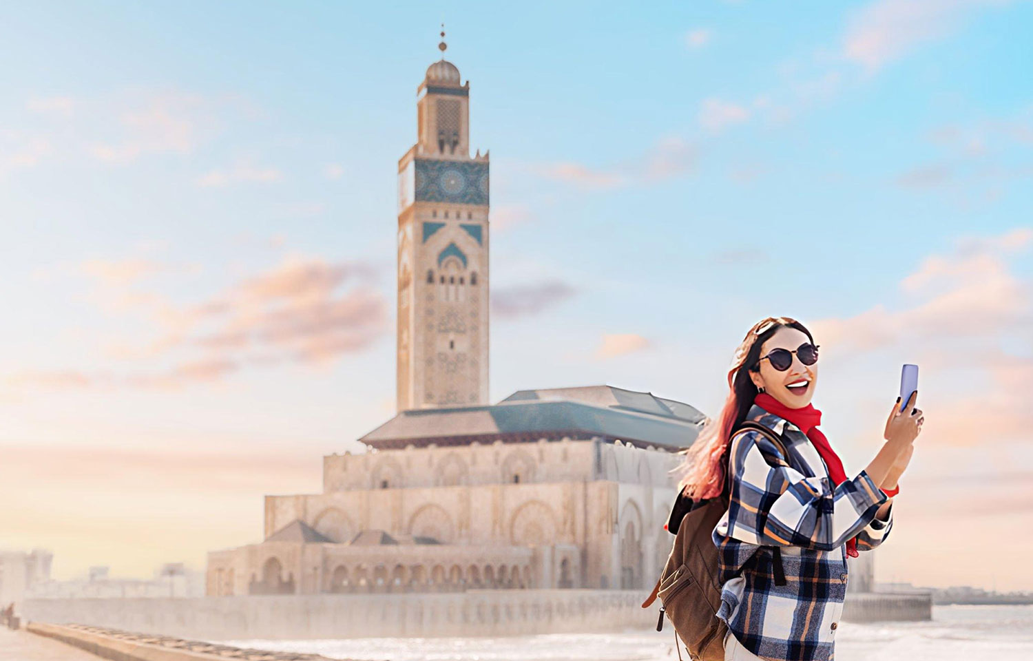a tourist capturing the stunning Hassan II Mosque by phone at sunset surrounded by the vibrant atmosphere of Casablanca