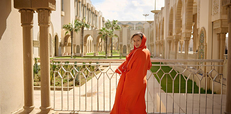 a woman with head covered in a head scarf at a mosque smiling looking at camera through her shoulders