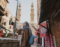 A vibrant street scene in what appears to be Old Cairo, with traditional architecture and a mosque dome, characteristic of archaeological tours in Egypt and Egypt archaeological trips.
