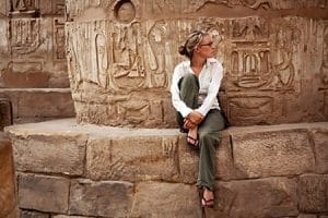 A person is intently observing ancient Egyptian hieroglyphs and carvings on a massive column within the Karnak Temple Complex, a quintessential scene from archaeological tours of Egypt and Egypt archaeological vacations.