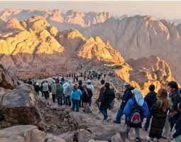 best-dahab-day-trip-to-mount-sinai A group of tourists hikes up a rocky mountain path at sunrise, suggesting a mountain safari or trek, a popular Dahab safari day tour and one of many Dahab Egypt activities.