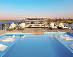 A pristine swimming pool on the deck of a luxury Nile River cruise ship, with lounge chairs and the river in the background. Best Luxury Nile River Cruise.