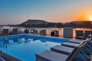 A swimming pool and lounge chairs on the top deck of a Nile cruise ship at sunset, with the calm river and distant hills in the background, representing the relaxing amenities on best standard Nile cruises.