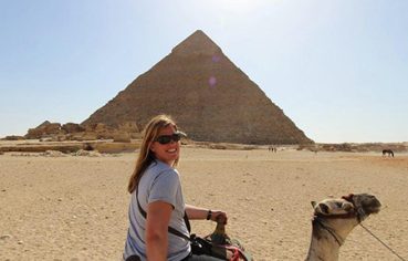 A happy tourist riding a camel with the Great Pyramid of Giza in the background during a budget Egypt tour covering Cairo, Luxor, Aswan, and Hurghada over 9 days.