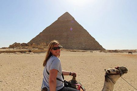 A Happy Tourist Riding A Camel With The Great Pyramid Of Giza In The Background During A Budget Egypt Tour Covering Cairo, Luxor, Aswan, And Hurghada Over 9 Days.