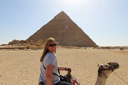 A happy tourist riding a camel with the Great Pyramid of Giza in the background during a budget Egypt tour covering Cairo, Luxor, Aswan, and Hurghada over 9 days.