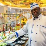 Smiling cruise chef standing proudly next to a beautifully arranged fresh salad buffet.