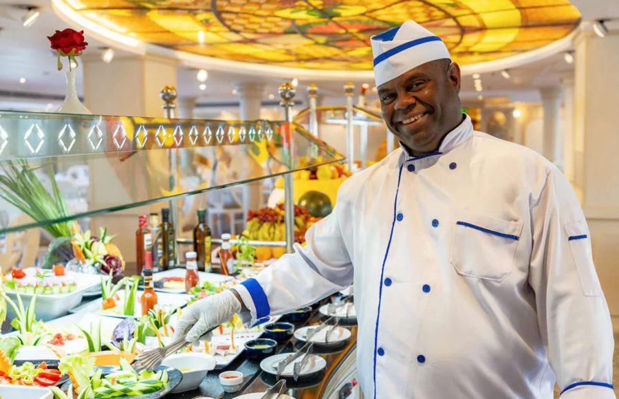 Smiling cruise chef standing proudly next to a beautifully arranged fresh salad buffet.