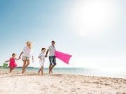 A family of four, parents and two young children, happily walk hand-in-hand along a white sand beach with an inflatable raft, illustrating a perfect family-friendly stop on a cairo luxor hurghada tour.