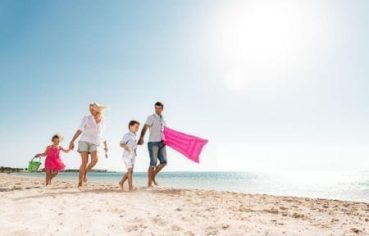 A family of four, parents and two young children, happily walk hand-in-hand along a white sand beach with an inflatable raft, illustrating a perfect family-friendly stop on a cairo luxor hurghada tour.