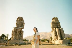 A traveler standing in front of the two massive seated statues of the Colossi of Memnon in Luxor, Egypt, with desert mountains in the background, is a highlight of a 3 day Egypt itinerary