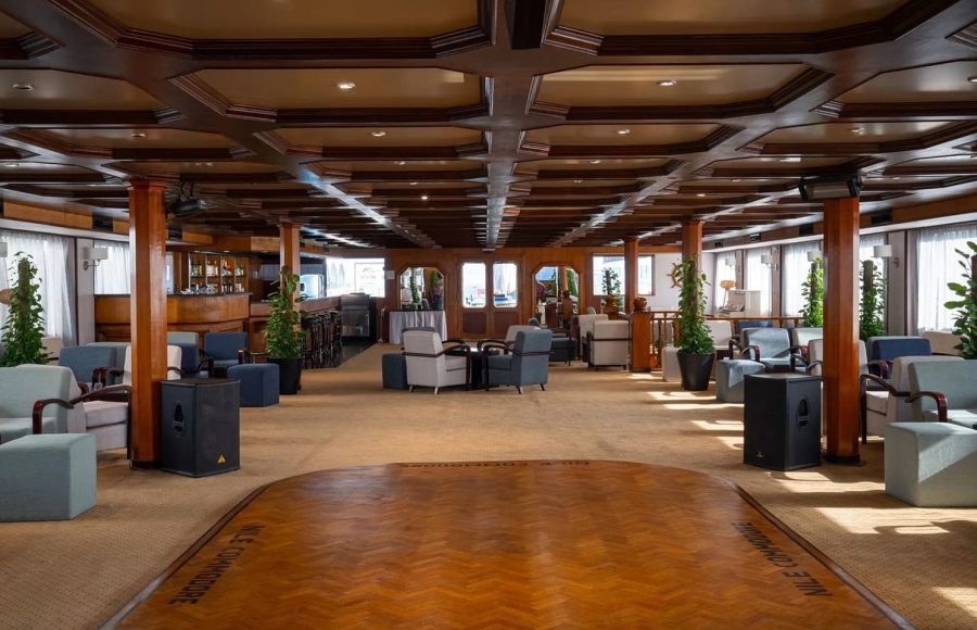 Spacious and richly decorated reception and Alt Text: Spacious, wood-paneled lounge and dance floor area on Alt Text: Large, elegant lounge and reception area with a wooden ceiling and seating on the MS Commodore Nile Cruise boat.