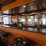 Luxurious wood-paneled bar with black stools Alt Text: Close-up of the polished wooden bar with leather stools on the MS Commodore Nile Cruise boat.