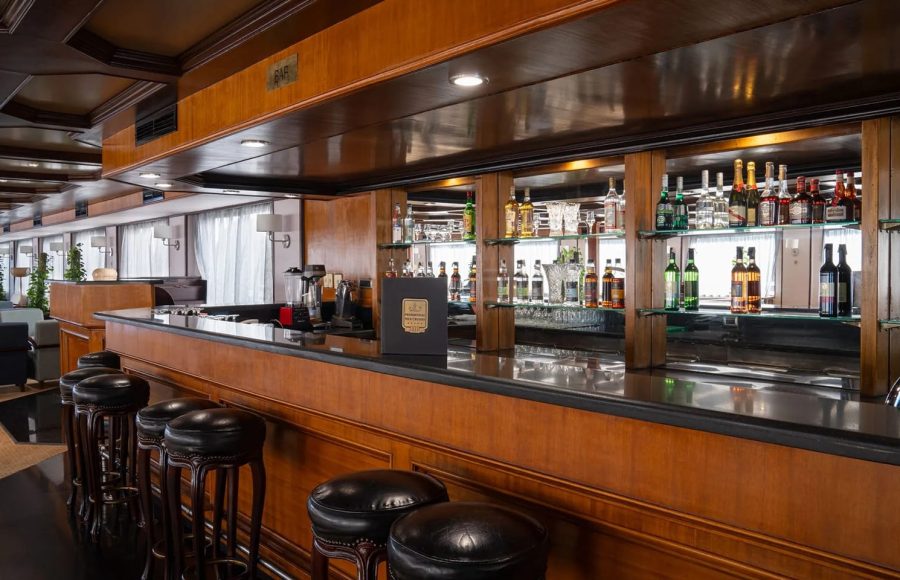 Luxurious wood-paneled bar with black stools Alt Text: Close-up of the polished wooden bar with leather stools on the MS Commodore Nile Cruise boat.