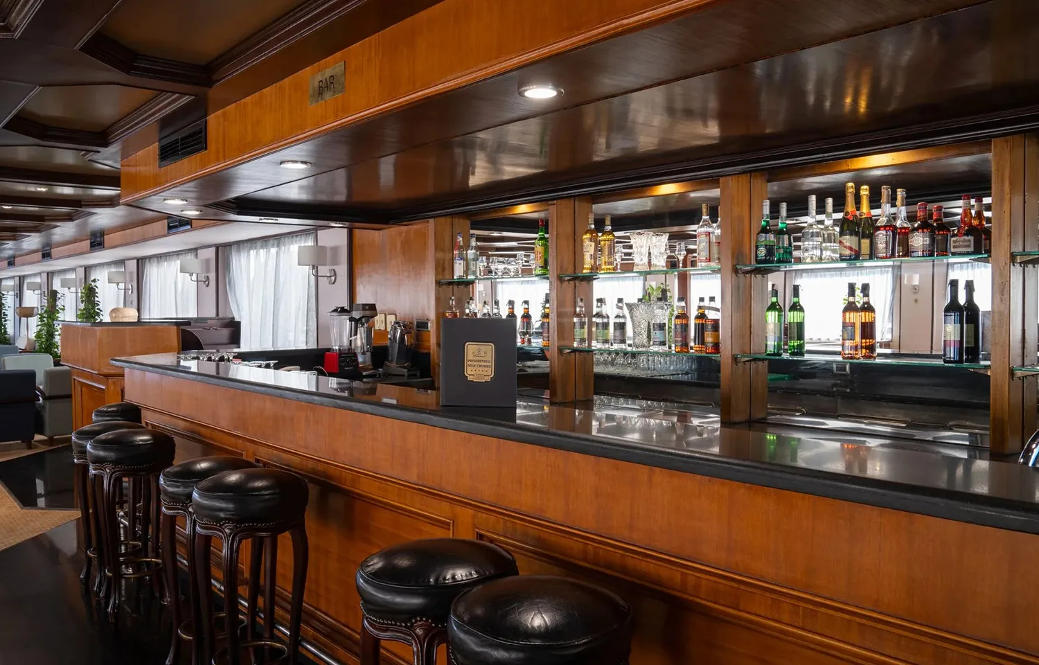 Luxurious wood-paneled bar with black stools Alt Text: Close-up of the polished wooden bar with leather stools on the MS Commodore Nile Cruise boat.
