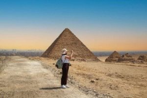 A tourist facing away from the camera towards the Giza Pyramids in the desert, a classic scene on Egypt overland tour packages.
