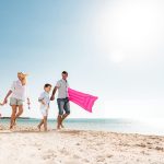 A happy family walk barefoot along a sunny sandy beach with calm blue water at their 6 days Cairo and Hurghada Holiday.