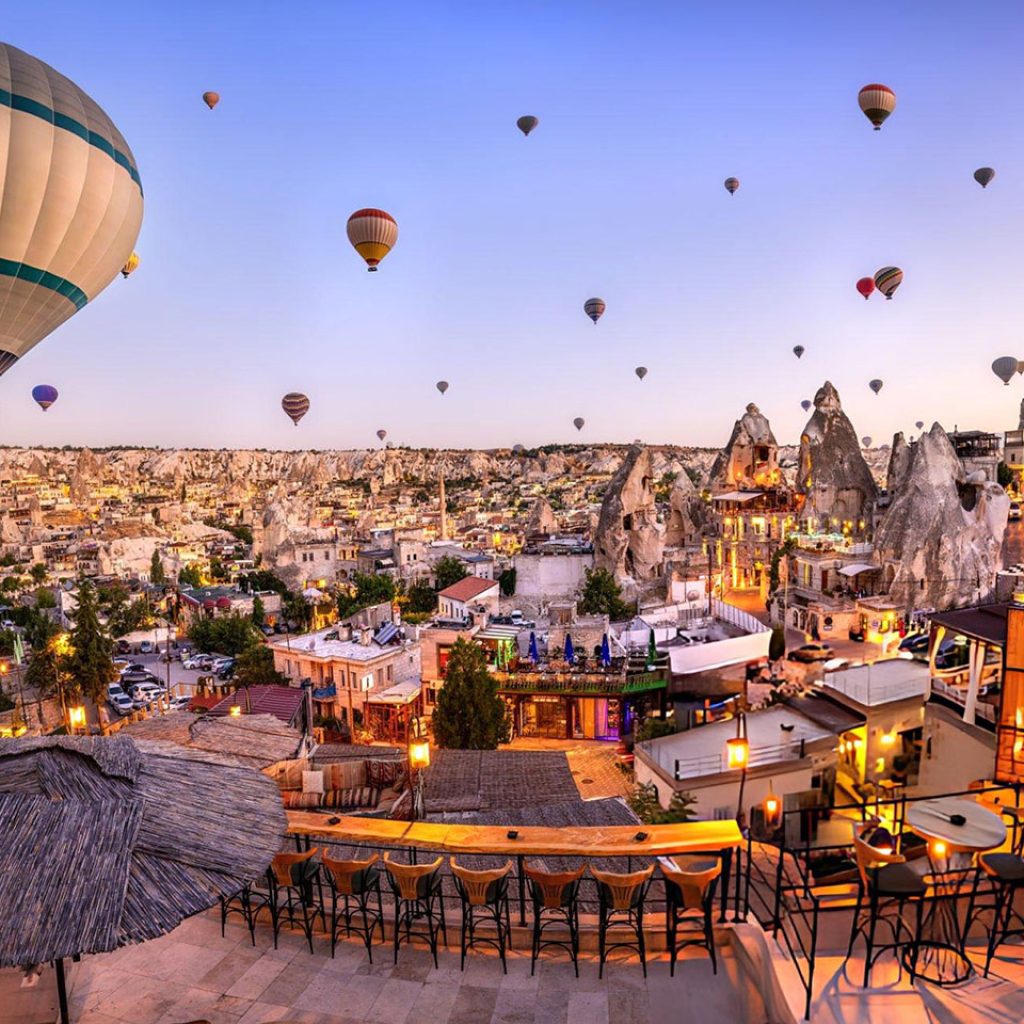 hot air balloons creating an iconic travel scene over Goremes unique fairy chimney landscape and illuminated village buildings in Cappadocia Turkey at dawn
