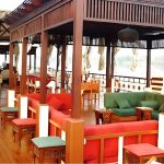 Spacious wooden upper deck of a Dahabiya boat with colorful lounge seating and a shaded canopy.