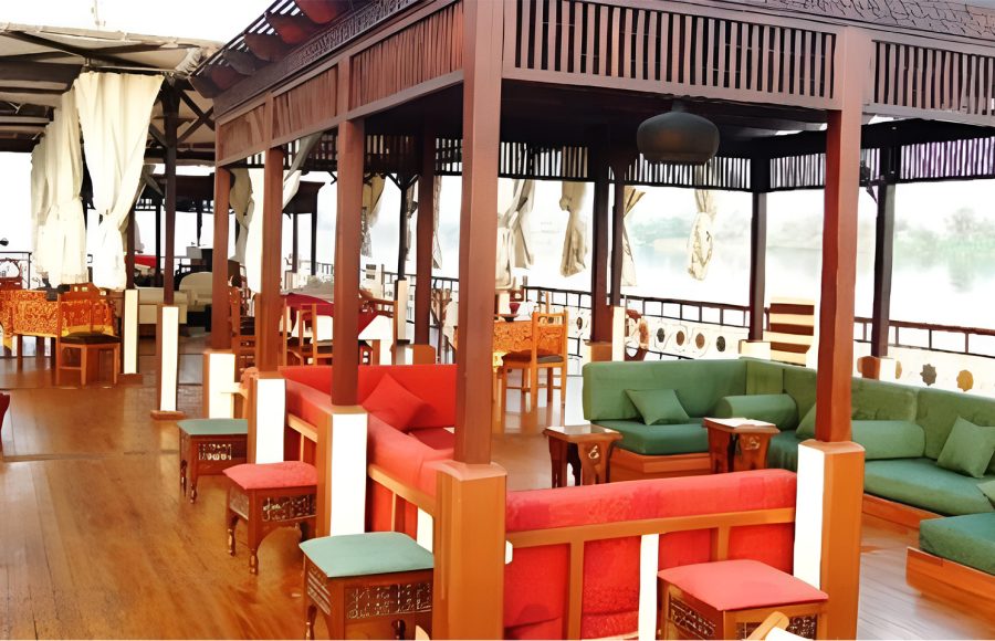 Spacious wooden upper deck of a Dahabiya boat with colorful lounge seating and a shaded canopy.