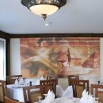 Elegant indoor dining room with white-clothed tables and a large abstract wall mural.