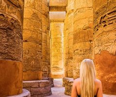 Blonde woman admiring the massive, hieroglyph carved columns inside the Great Hypostyle Hall of Karnak Temple in Luxor, Egypt, a highlight of a 3 day Egypt itinerary.