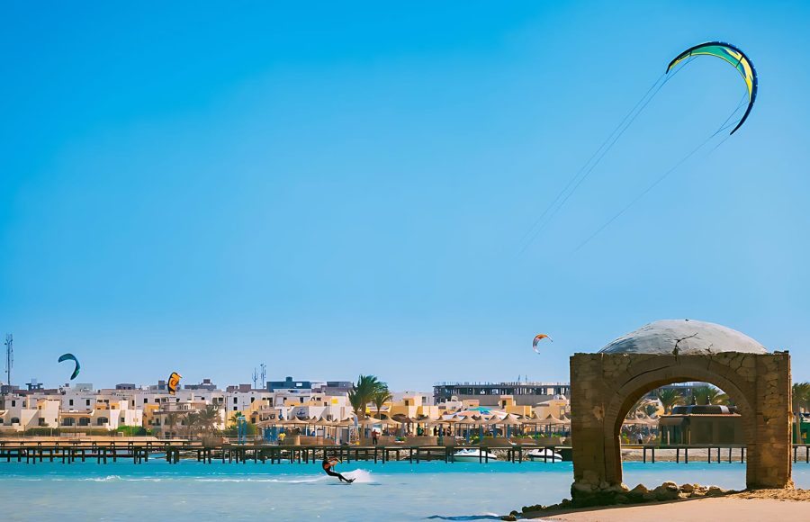 A kite surfer moving quickly through the shallow blue water near a beach.