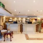 Wood-paneled cruise suite seating area with television, minibar, and queen bed visible.