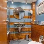 Ship cabin bathroom with wood paneling, circular mirror, and vessel sink.
