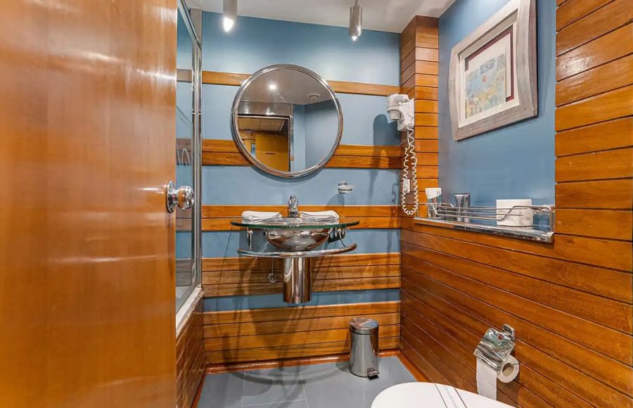 Ship cabin bathroom with wood paneling, circular mirror, and vessel sink.