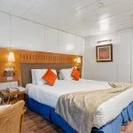 Cruise ship cabin with double bed, wooden headboard, and sliding balcony door.