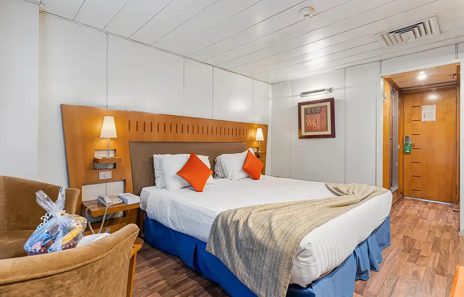 Cruise ship cabin with double bed, wooden headboard, and sliding balcony door.