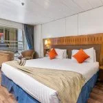 Cruise ship cabin with double bed, wooden headboard, and sliding balcony door.