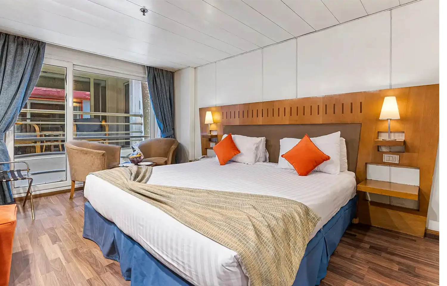 Cruise ship cabin with double bed, wooden headboard, and sliding balcony door.