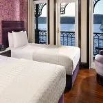 A luxurious twin-bed cabin on the mövenpick ss misr steamer cruise with a balcony door open to a beautiful view of the River Nile.