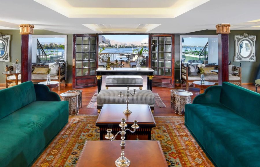 The opulent Lounge on the Mövenpick SS Misr cruise with plush seating and doors opening to the panoramic views of the Nile.