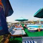 Outdoor high-top tables and lounge seating on a cruise ship deck at sunset.