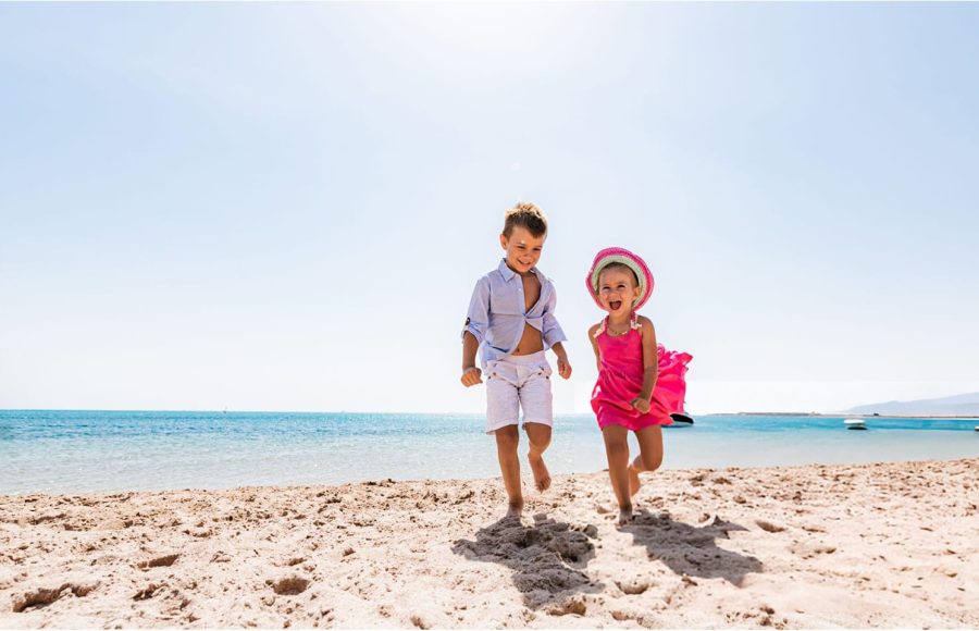 Boy and girl laughing and running barefoot on the Red Sea beach.
