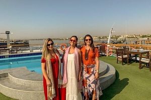 Three women smiling on the deck of a Nile River cruise ship with a swimming pool and river view in Egypt.