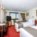 Traditional-style twin cabin on a Nile cruise with two beds, red patterned carpet, dark wood furniture, and a window view of the river.