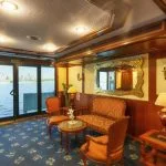Curved bar area on a cruise ship with brown leather bar stools, a polished granite counter, and shelves of liquor bottles.