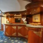 Curved, polished wood reception desk with marble countertops and traditional Egyptian decor in the ship's lobby.